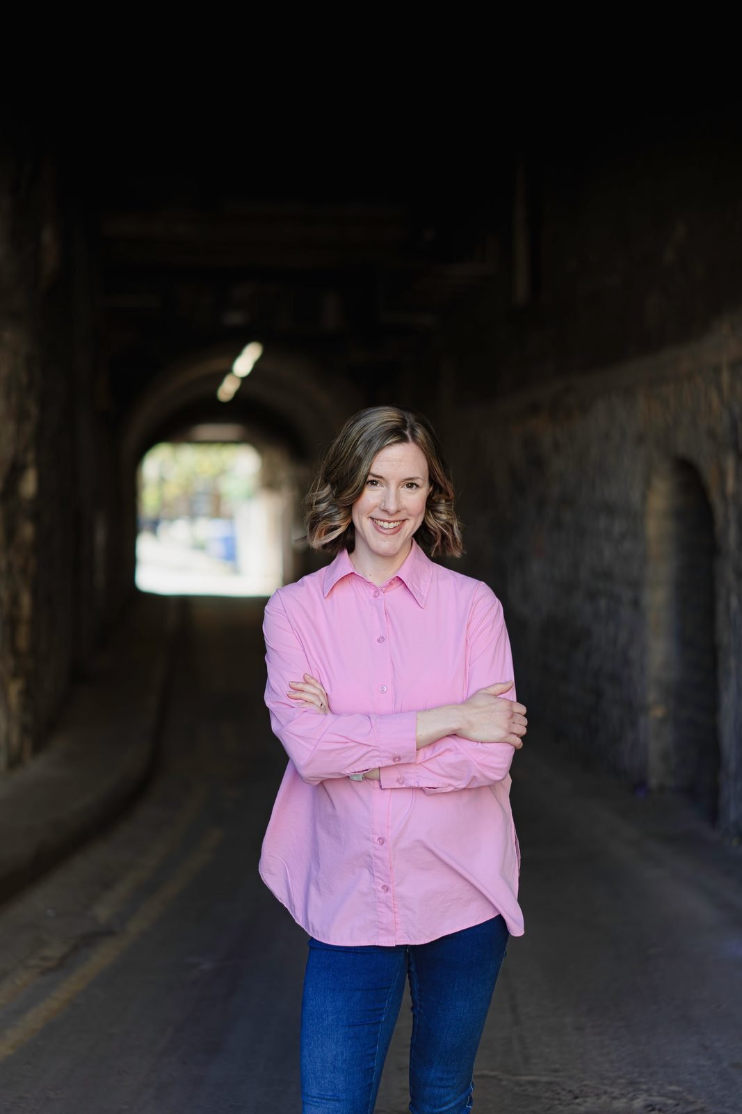 Liv standing with arms folded in a stone passageway in Bath